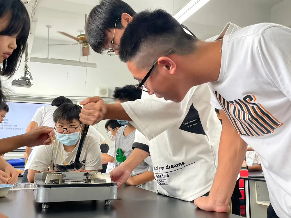 志工俯身在爐火上攪動糖漿,孩子們專心看著