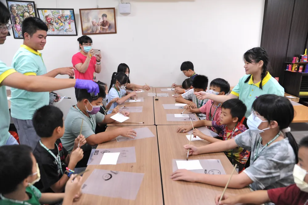 孩子們坐在長桌邊,在透明片上用水彩筆畫出自己的圖案